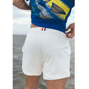 Man wearing cream lounge shorts and blue shirt with ocean water in background.