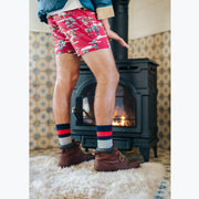 Man standing in room next to fireplace wearing jacket, red underwear, and chunky knit stripe socks.