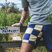 Man wearing half checkered half solid blue and white mesh lounge shorts sitting on a sign that says private property.