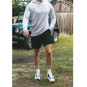 Man standing in front of blue jeep wearing light linen stripe hoodie, black lounge shorts, and blue/red stripe varsity socks.