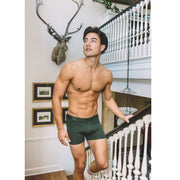 Shirtless man walking up stairs in home wearing olive boxer briefs.
