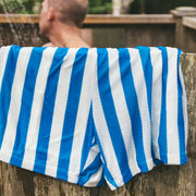 Man standing in outdoor shower with blue and white cabana stripe lounge shorts hanging over side of shower.