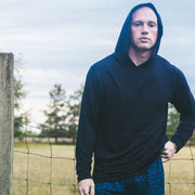 Man standing in field in front of fence wearing a black hoodie.