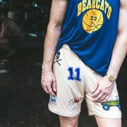 Man standing in doorway wearing blue basketball shirt and beige lounge short that says "cash rules everything around me" with various icons like 11 patch, truck, football, skull and bones etc.