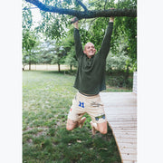 Man hanging on a tree smiling wearing Beige lounge short that says "cash rules everything around me" with various icons like 11 patch, truck, football, skull and bones etc. 