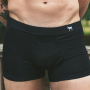 Close up shot of shirtless man wearing black boxer briefs with white goat monogram on waistband.
