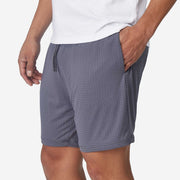 Close up of man wearing grey mesh short with hand in pocket.
