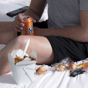 Man eating chinese food on his bed in pocket lounge shorts.
