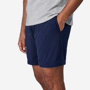 Close up shot of man wearing navy blue lounge short with hand in pocket.
