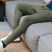 Man wearing matte olive lounge pants on a grey couch.