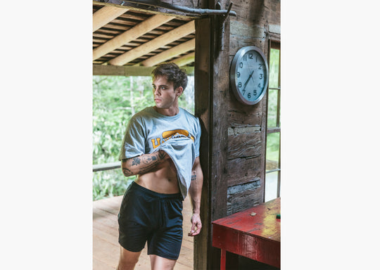 Man inside of cabin wearing black lounge shorts and grey t-shirt.