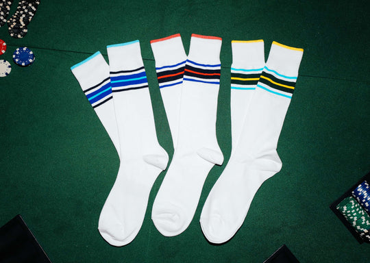 3 pairs of white Amalfi Athletic socks with stripes on the cuff in various colors sitting on green felt poker table