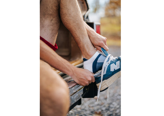 Close up of man putting on shoe over blue/white performance ankle sock.
