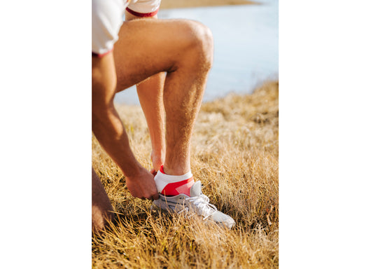 Close up shot of man putting on shoe wearing white/red performance ankle socks.