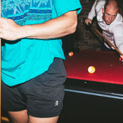 Man leaning on red pool table in lounge shorts with skully embroidery.