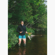 Man standing in water fishing wearing boxers and a black hoodie