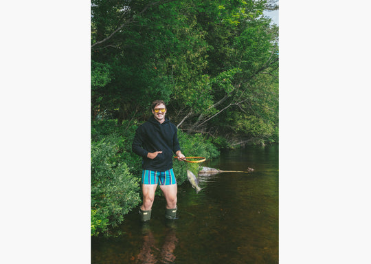 Man standing in water fishing wearing boxers and a black hoodie