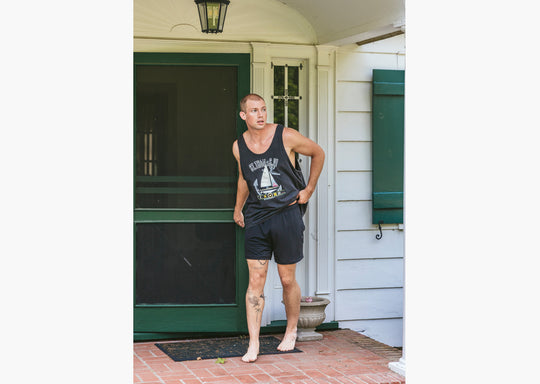 Man standing on stoop wearing black tank top and black lounge shorts.
