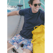Man sitting on boat smiling wearing blue shirt and blue madras print lounge shorts.