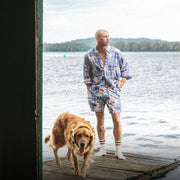 Man in Madras lounge shorts with dog on dock.
