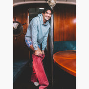 Man on boat stepping into red jeans and also wearing grey sweatshirt and blue madras slim fit boxers