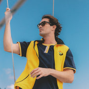Man wearing a yellow and navy shirt with sunglasses against a blue sky.
