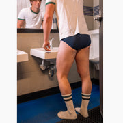 Man standing in bathroom in front of sink wearing white t-shirt and navy blue briefs.