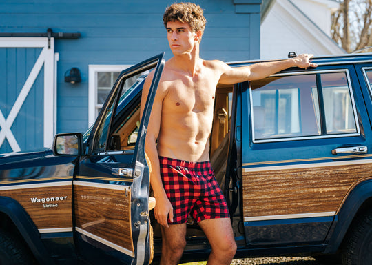 Shirtless man standing in front of a wagoneer wearing red/black buffalo plaid slim fit boxers.