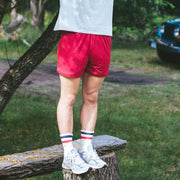 Man standing on wooden bench wearing grey t-shirt and burgundy lounge shorts.
