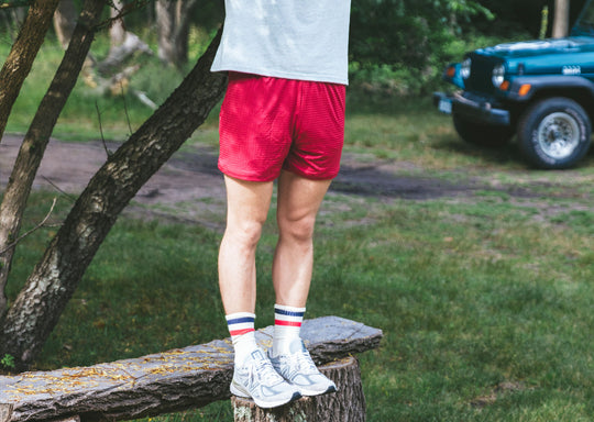 Man standing on wooden bench wearing grey t-shirt and burgundy lounge shorts.