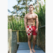 Shirtless man walking on wood path wearing burgundy/white beach patrol lounge short.