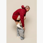 Man standing in studio putting on grey sweat pants and also wearing burgundy boxer briefs and oodie.