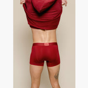 Backshot of standing in studio taking off burgundy sweatshirt and wearing burgundy boxer briefs. 