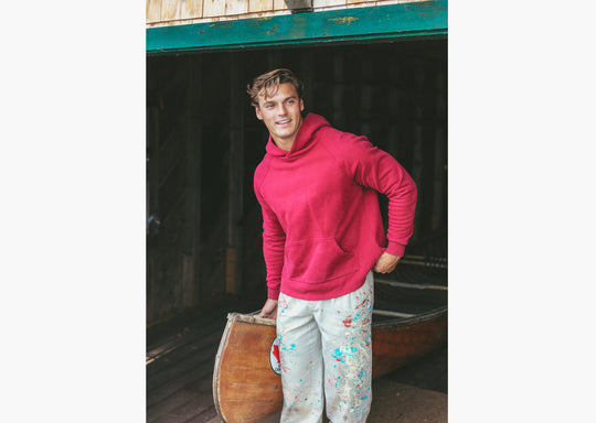 Close up of man in boathouse next to canoe wearing burgundy hoodie
