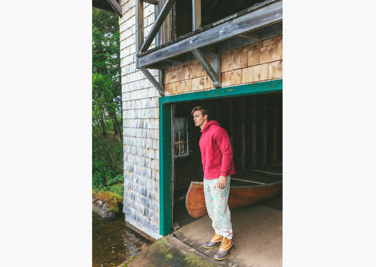Man sitting in boathouse next to canoe wearing burgundy hoodie