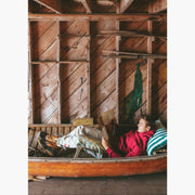 Man sitting in a canoe reading wearing burgundy hoodie