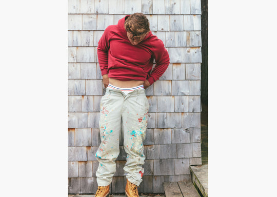 Man standing next to wooden wall wearing burgundy hoodie
