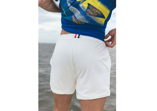 Man wearing cream lounge shorts and blue shirt with ocean water in background.