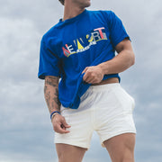 Man wearing blue shirt and cream lounge shorts with blue sky in background. 