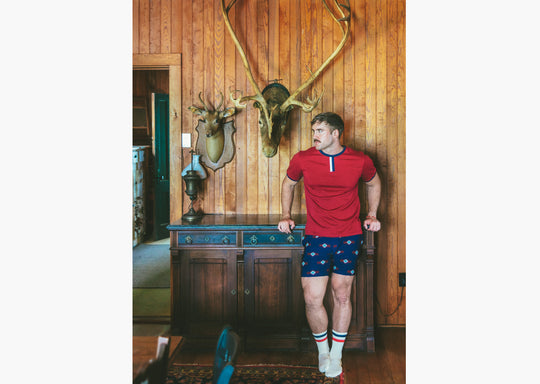 Man standing in house with wood walls wearing burgundy vintage ringer shirt