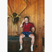 Man sitting in house with wood walls on phone wearing burgundy vintage ringer shirt