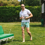 Man standing in a grassy area wearing a white shirt and green and white striped slim fit boxers.