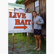 Man wearing cabin club lounge shorts and grey hoodie. He is standing next to large sigh that says live bait 