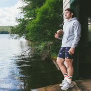 Man standing in boat garage holding football wearing grey hoodie and navy Cabin Club lounge shorts