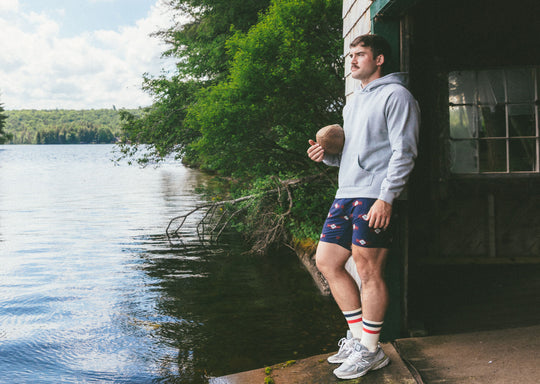 Man standing in boat garage holding football wearing grey hoodie and navy Cabin Club lounge shorts