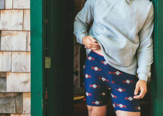 Man wearing Cabin Club lounge shorts and grey hoodie standing in doorway