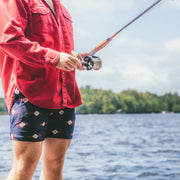 man standing on dock fishing wearing red long sleeve shirt and navy Cabin Club lounge shorts
