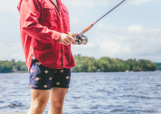 man standing on dock fishing wearing red long sleeve shirt and navy Cabin Club lounge shorts