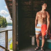 Shirtless man in boathouse wearing Canoe Stripe lounge shorts. Lake in background.