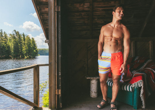 Shirtless man in boathouse wearing Canoe Stripe lounge shorts. Lake in background.